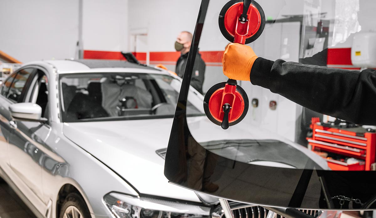 Detailaufnahme. Hand eines Mitarbeiter einer kfz-Werkstatt trägt  eine Windschutzscheibe per Doppelsauger.