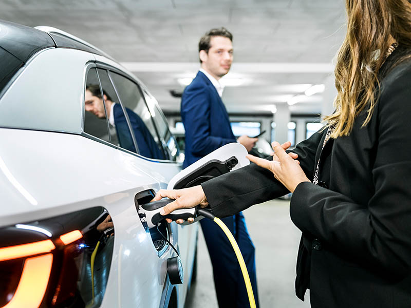 E-Auto lädt in der Tiefgarage. Eine Mann und eine Frau unterhalten sich über den Stromverbrauch des E-Autos