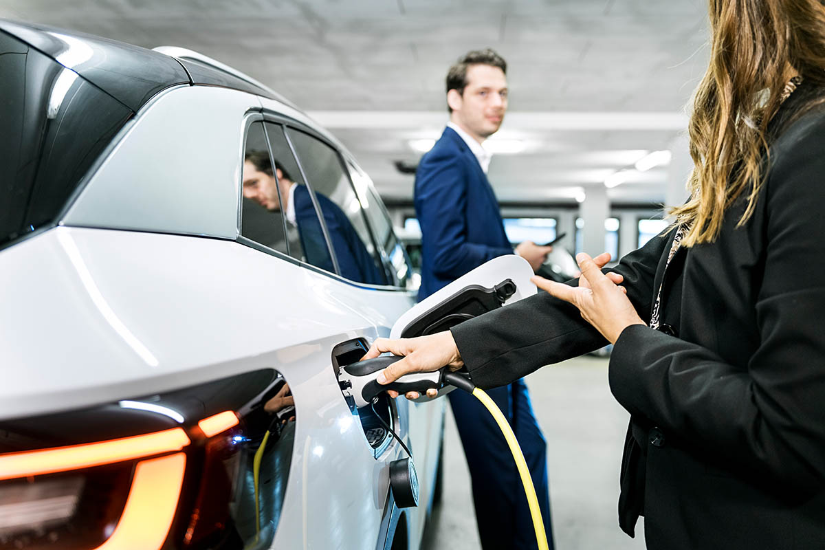 E-Auto wird in Tiefgarage mit AC von einer Frau geladen, die sich mit einem Mann unterhält