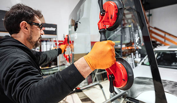 Mitarbeiter einer Kfz-Werkstatt tauscht Windschutzscheibe im Zuge einer Glasschaden-Reparatur